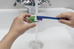 Hands gently brushing a dental retainer under running water, showing how to clean retainers safely 