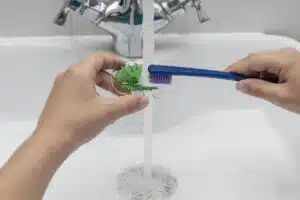 Hands gently brushing a dental retainer under running water, showing how to clean retainers safely