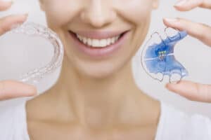 Smiling patient holding clear and removable retainers, highlighting proper retainer maintenance for lasting alignment 