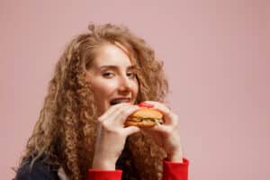 Young woman with braces biting into a burger, showing what not to eat with braces