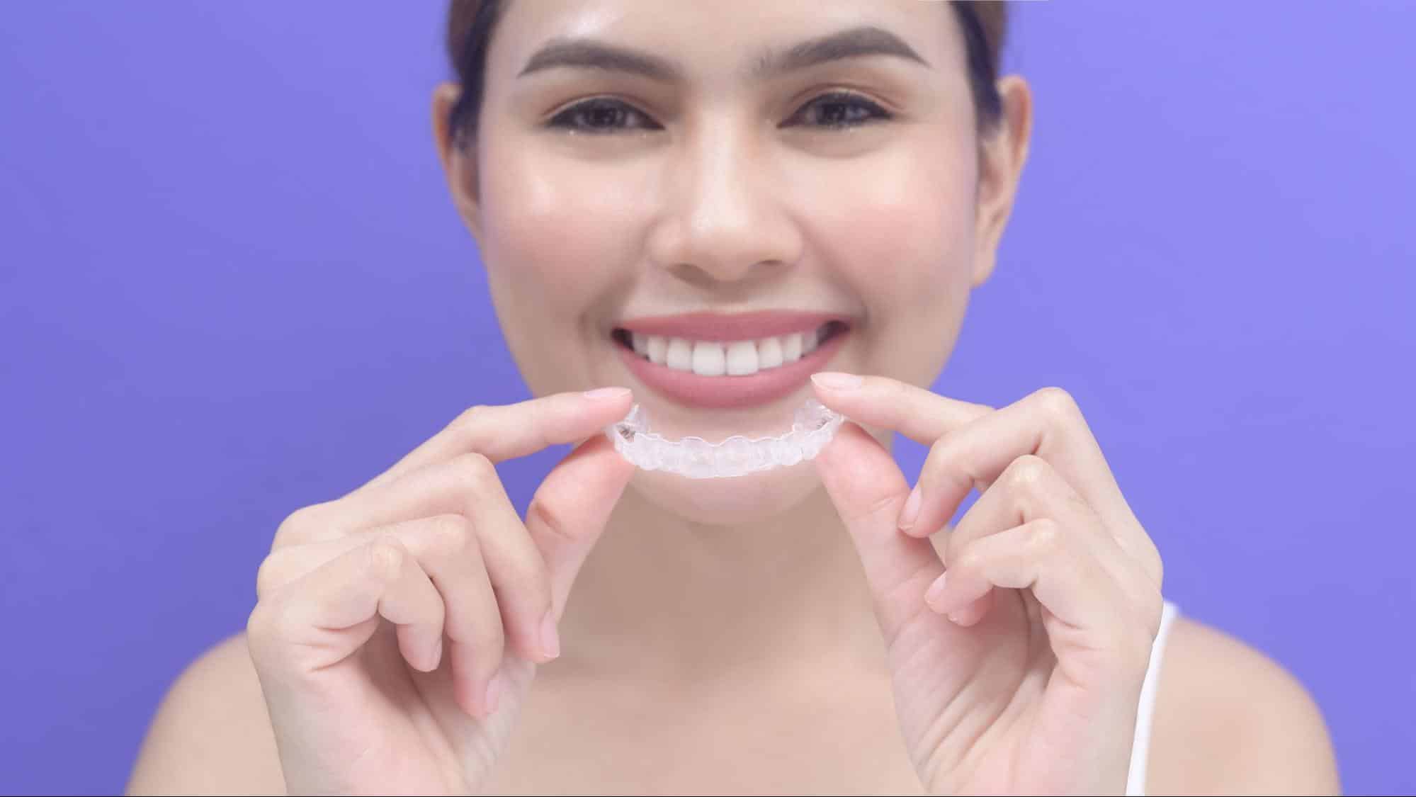 Smiling woman holding a clear aligner and its carrying case.