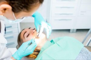 An orthodontist wearing blue gloves placing a clear aligner tray on a female patient’s teeth