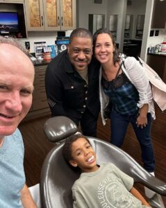 A young boy smiling in a dental chair surrounded by his parents and a doctor at Goodman Orthodontics