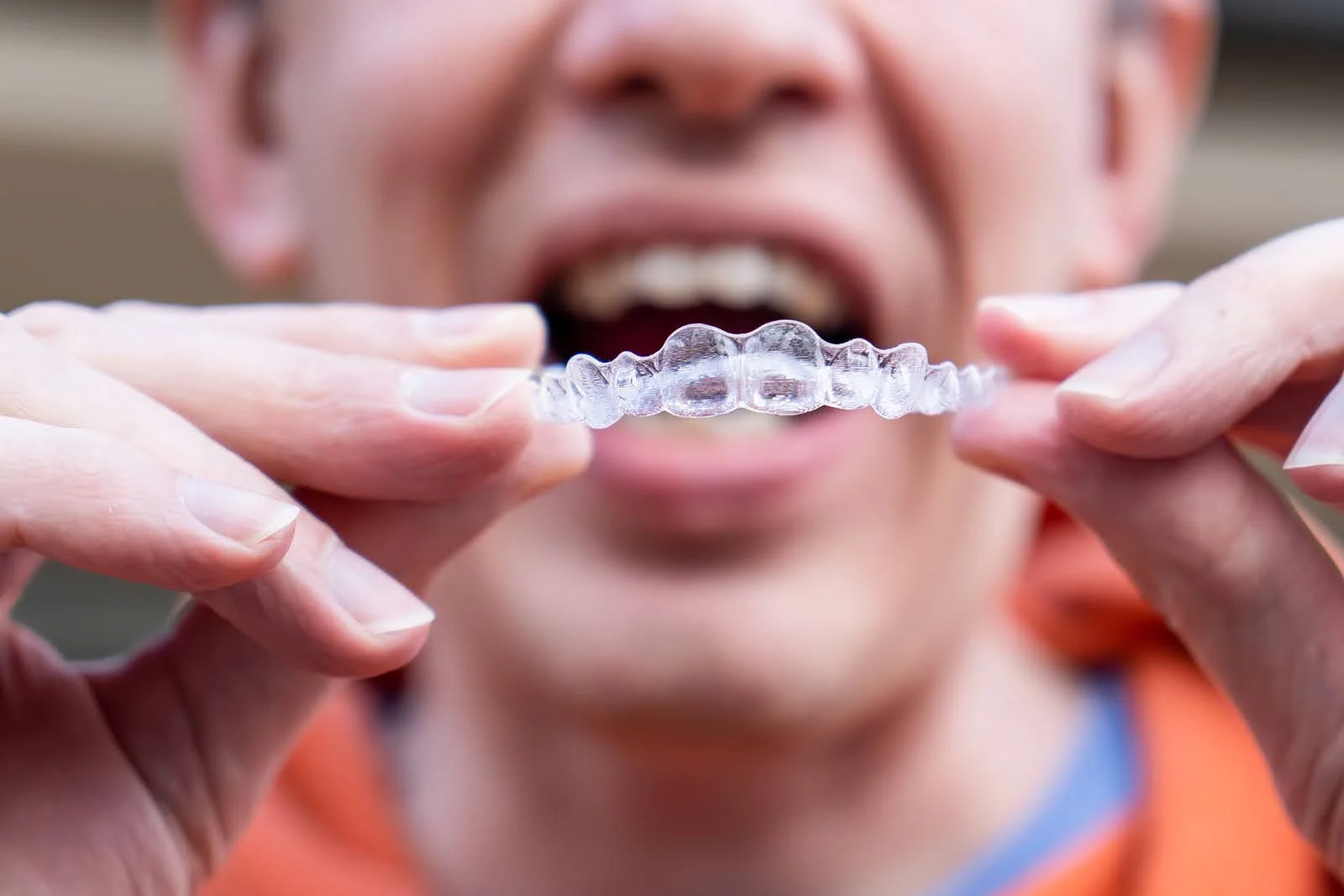 Adult holding a clear aligner illustrating Invisalign treatment for adults