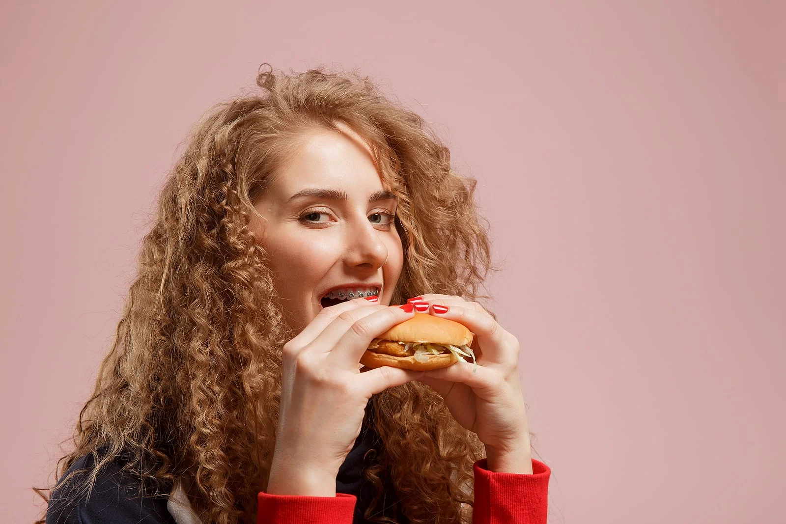 Young woman with braces biting into a burger, showing what not to eat with braces